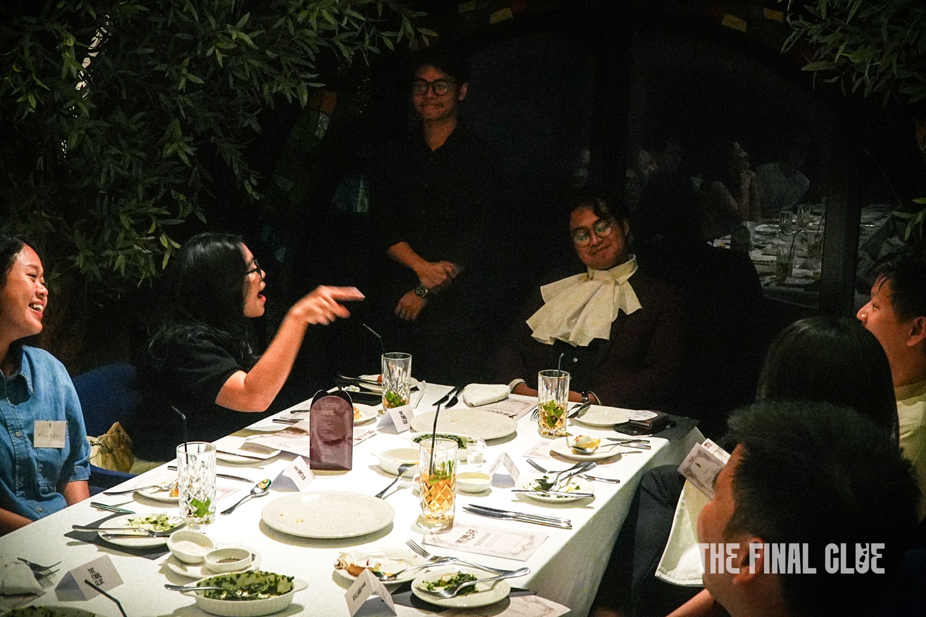 Guests seated around a set dinner table at a Final Clue murder mystery night, plates and clue cards in front of them.